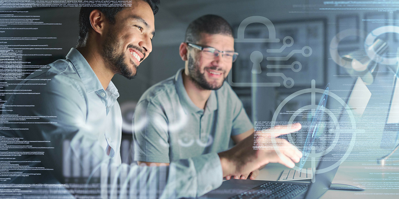 two men point at a laptop screen while smiling