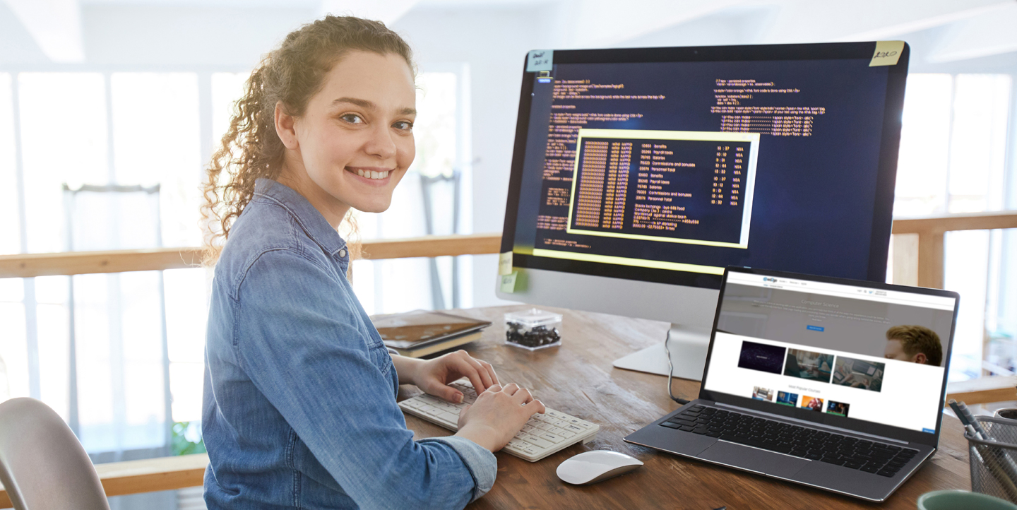 female coding at a computer but looking at the camera